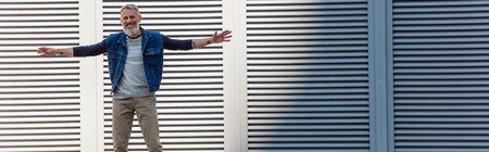 tattooed and happy middle aged man with outstretched hands riding longboard on urban street, bannerの写真素材