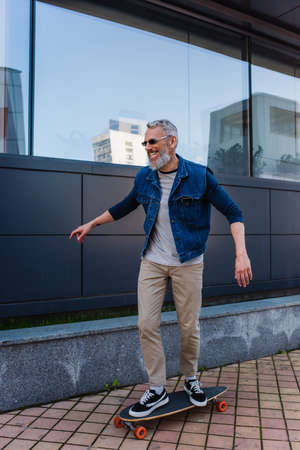 full length of cheerful and mature man riding longboard on urban streetの写真素材