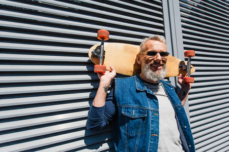 bearded middle aged man in sunglasses smiling and holding longboardの写真素材