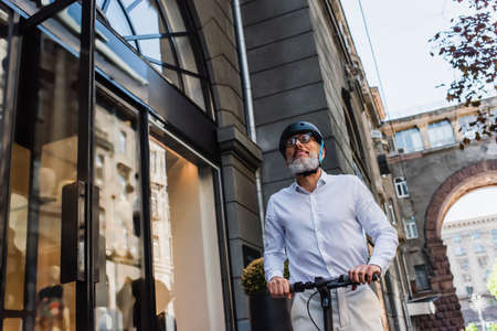 low angle view of mature man in shirt and helmet riding electric scooter