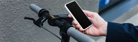 cropped view of mature businessman holding smartphone with blank screen near e-scooter, banner