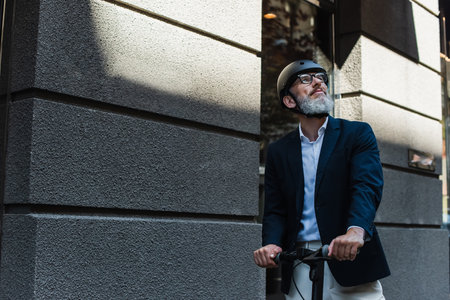 mature businessman in blazer and helmet riding electric scooterの写真素材