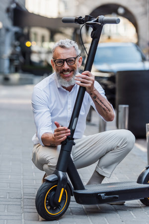 happy mature man adjusting electric scooter on streetの写真素材