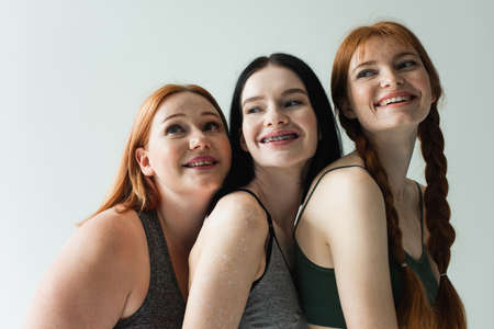 Happy body positive sportswomen looking away isolated on gray