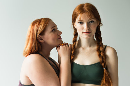 Plus size sportswoman looking at redhead friend isolated on grayの写真素材