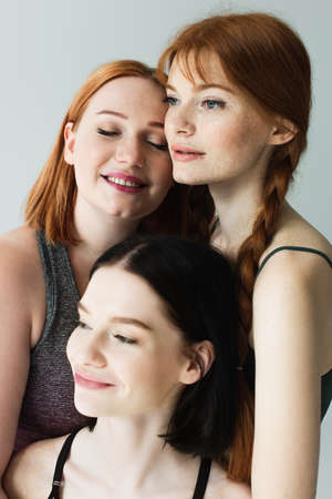 Smiling body positive sportswomen smiling and looking away isolated on grayの写真素材