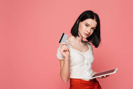 Woman with vitiligo holding digital tablet and credit card isolated on pink