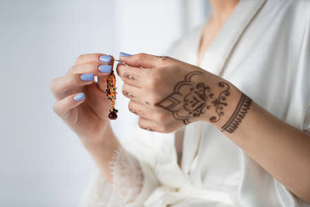 cropped view of indian woman with mehndi holding earring isolated on whiteの写真素材