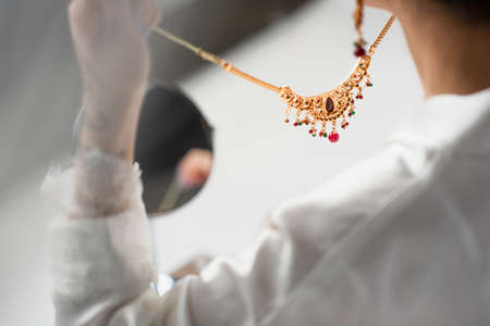 cropped view of young bride holding necklace on white