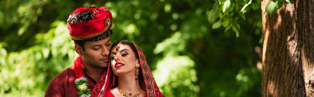 Indian man in turban looking at bride with mehndi in sari and headscarf, banner