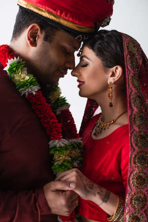 side view of smiling indian husband and wife in traditional clothing holding hands isolated on whiteの写真素材
