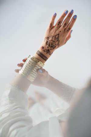 partial view of indian woman with mehndi wearing golden bracelet while getting ready to wedding on whiteの写真素材