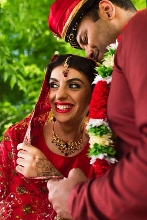 pleased indian man in turban hugging happy bride in red sariの写真素材