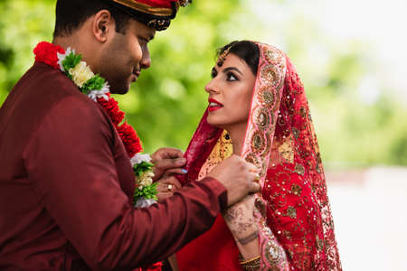 indian man adjusting headscarf on bride in sariの写真素材