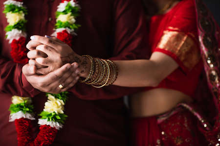 cropped view of indian man in floral garland holding hands with bride in traditional sariの写真素材