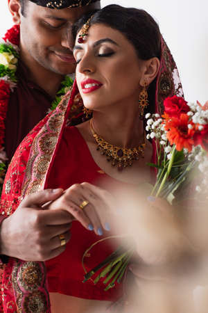 indian man holding hand of bride with ring on finger isolated on white