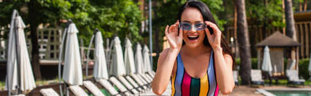 Excited woman in swimsuit and sunglasses looking at camera on resort, bannerの写真素材