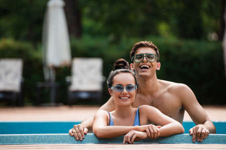 Shirtless man standing near girlfriend in swimming pool during vacationの写真素材