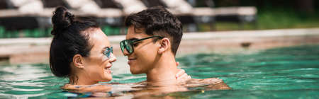 Side view of smiling woman touching neck of boyfriend in swimming pool, bannerの写真素材