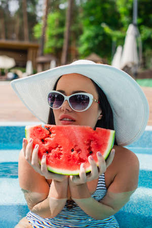 Young woman in sun hat holding tasty watermelon in swimming poolの写真素材