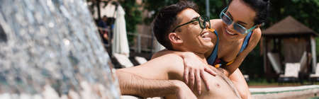 Woman in swimwear hugging boyfriend near blurred fountain on resort, bannerの写真素材
