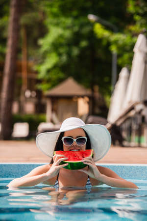 Young woman in swimming pool eating watermelon during vacationの写真素材