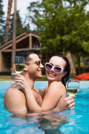 Cheerful man with wine looking at girlfriend in swimming poolの写真素材