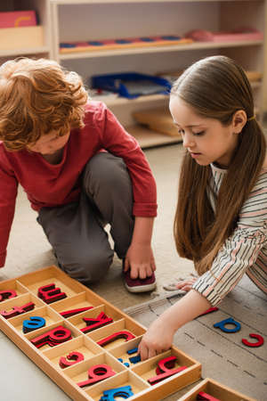 kids playing with wooden letters on floor in montessori school