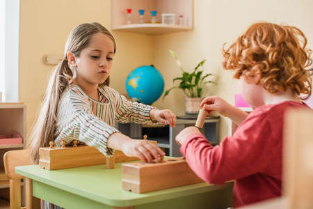 blurred redhead boy playing cognitive game with girl in montessori schoolの写真素材