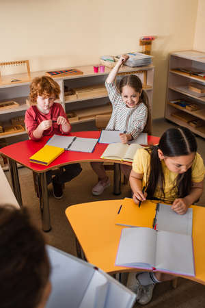 excited girl raising hand during lesson near interracial kids and blurred teacherの写真素材