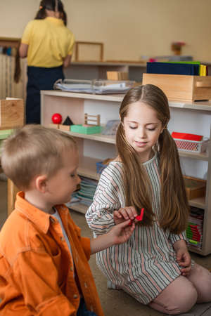 boy giving element of puzzle to girl sitting on floor in montessori school