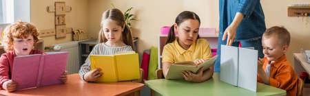 multicultural kids reading books near teacher in montessori school, bannerの写真素材
