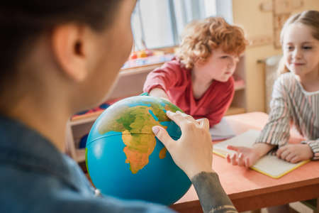 selective focus of globe in hands of teacher near kids in montessori schoolの写真素材