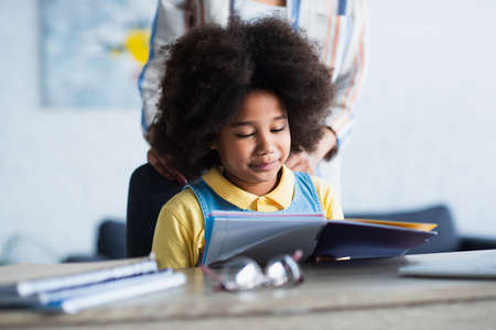 African american kid looking at notebook near blurred mother at homeの写真素材