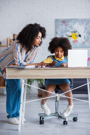 African american mother pointing at notebook near laptop and daughter at homeの写真素材
