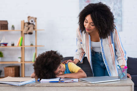 African american woman looking at sleeping daughter near notebook and laptopの写真素材