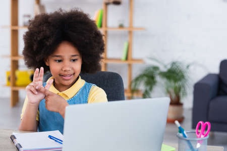 Smiling african american girl flexing fingers during online education on laptop