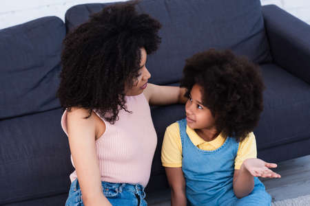 High angle view of young african american mother talking with daughter pointing with hand at home