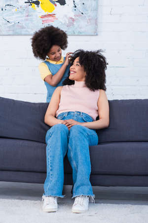 African american girl touching hair of mother on couch in living room