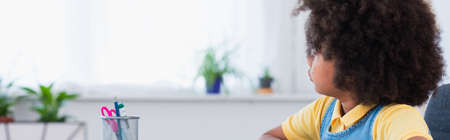 African american child looking away near stationery at home, banner