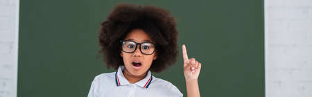 Amazed african american pupil having idea near chalkboard in school, bannerの写真素材