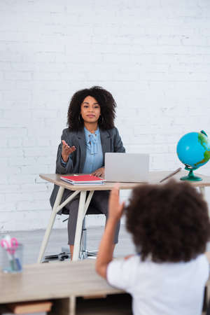 African american teacher pointing with hand at blurred pupil