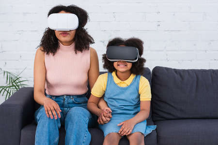 African american family in vr headsets holding hands on couch at home