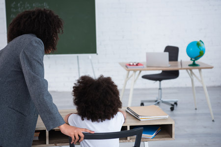 African american teacher standing near pupil in classroomの写真素材