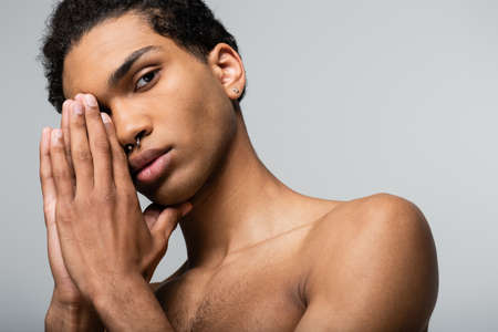 african american guy posing with hands near face while looking at camera isolated on gray, beauty conceptの写真素材