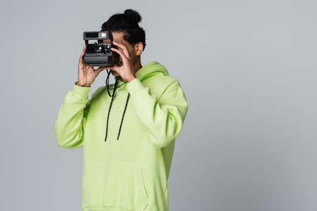 young african american man in green hoodie taking picture on vintage camera isolated on grayの写真素材