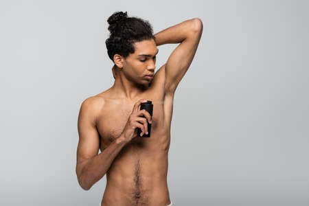 shirtless, young african american man spraying antiperspirant isolated on grayの写真素材