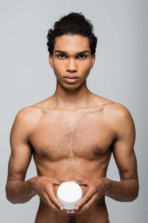 front view of shirtless african american man holding cosmetic cream isolated on grayの写真素材
