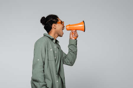 side view of stylish african american man screaming in megaphone isolated on grayの写真素材