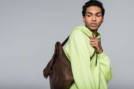 stylish african american man in green hoodie, with leather backpack isolated on gray